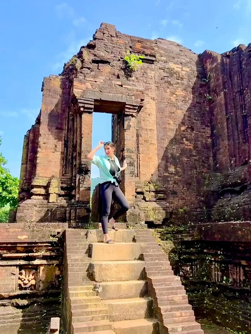 Một phụ nữ tạo dáng trên bậc thang gạch cổ giữa các tháp Chăm đổ nát tại thánh địa Mỹ Sơn.