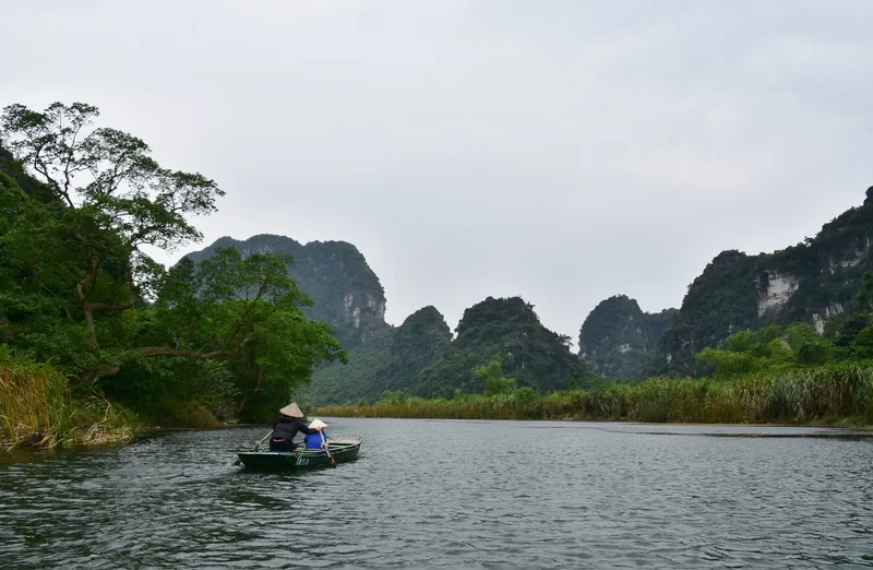 Một chiếc thuyền nhỏ lướt trên sông giữa những núi đá vôi tại Tràng An, Ninh Bình.